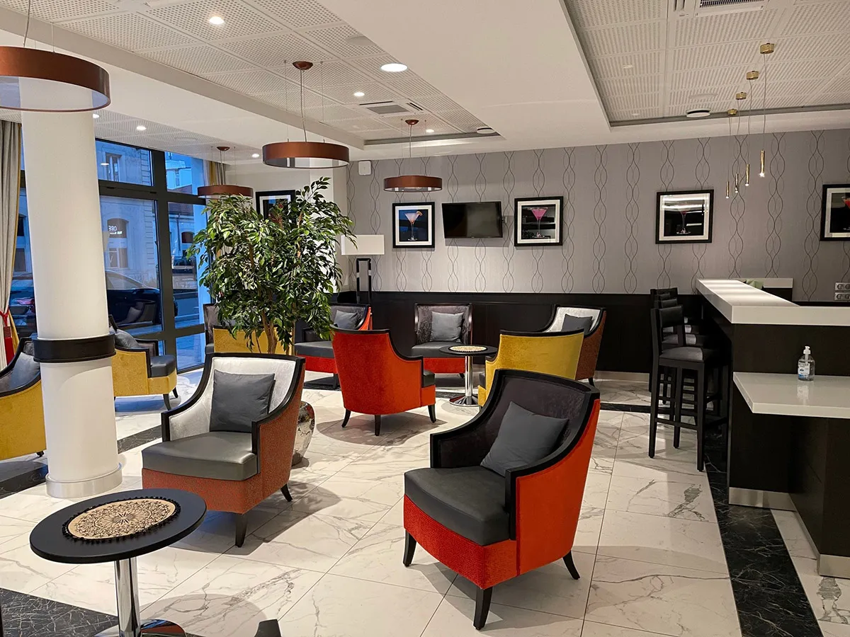 Salon-bar de la résidence seniors OBEO d'Aix-les-Bains : fauteuils rouge et jaune, comptoir de bar, sol en marbre et suspensions cuivrées