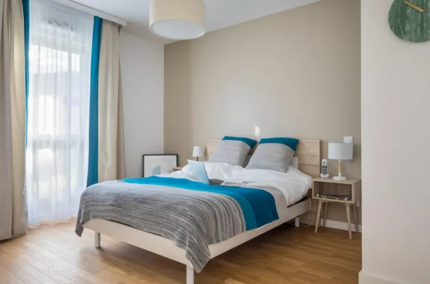 Chambre meublée : lit double, linge bleu et gris, tables de chevet et parquet clair