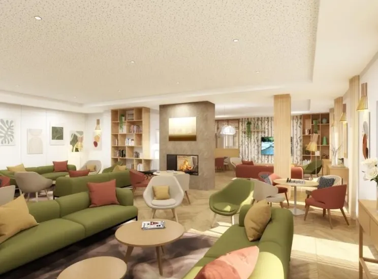 Grand salon de la résidence seniors OBEO à Éragny-sur-Oise : canapés verts et fauteuils terracotta autour de la cheminée, bibliothèque et coin télévision baignés de lumière