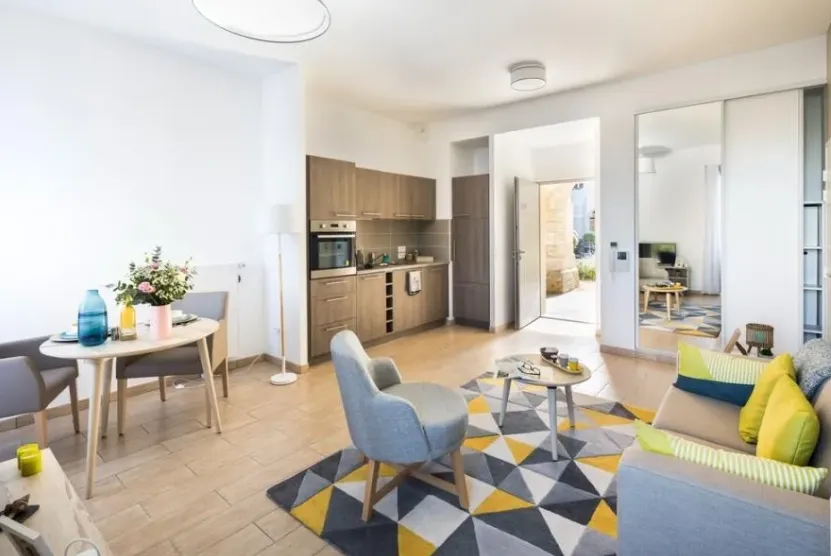 Studio meublé de la résidence OBEO d’Éragny-sur-Oise : coin repas, cuisine équipée ouverte, fauteuils bleus et tapis graphique