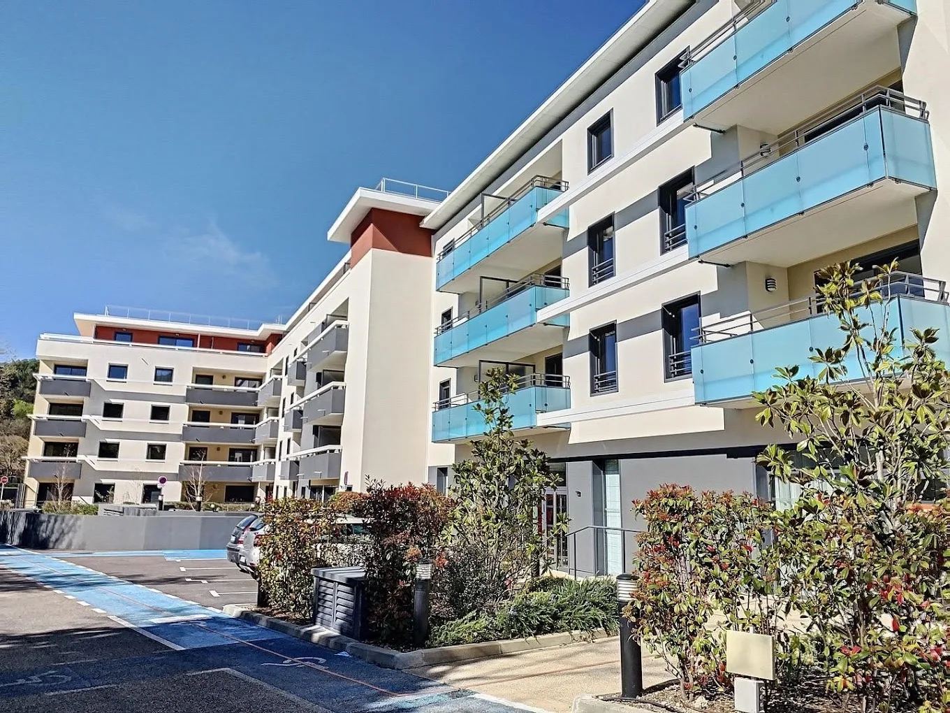 La résidence OBEO du Cannet vue du jardin : façade blanche à balcons bleus et allée bordée d’arbustes méditerranéens sous un ciel dégagé