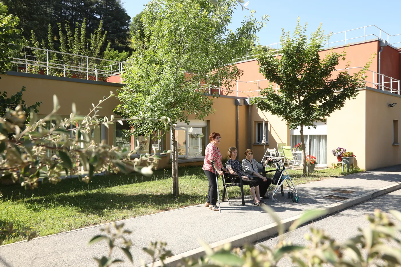 Résidents installés dehors autour d’une table, au milieu des arbres, devant la résidence