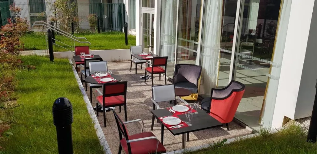 Terrasse extérieure de la résidence OBEO de Montreuil : tables et fauteuils colorés le long d’une bande de pelouse, devant les baies vitrées