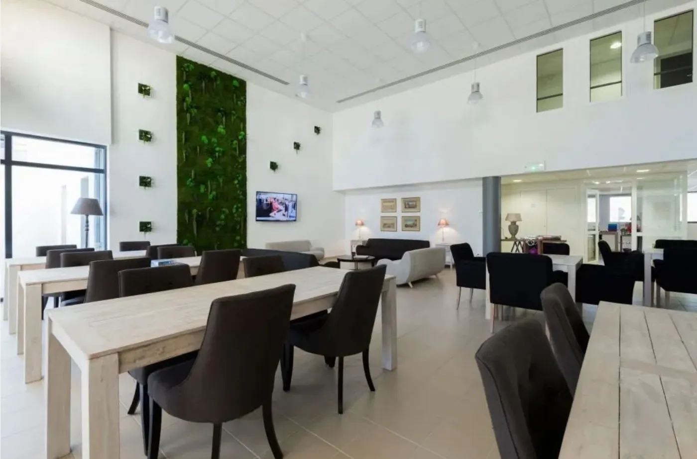 Salon-restaurant lumineux de la résidence services seniors OBEO à Nevers, avec mur végétal, grandes tables en bois clair et coin salon convivial