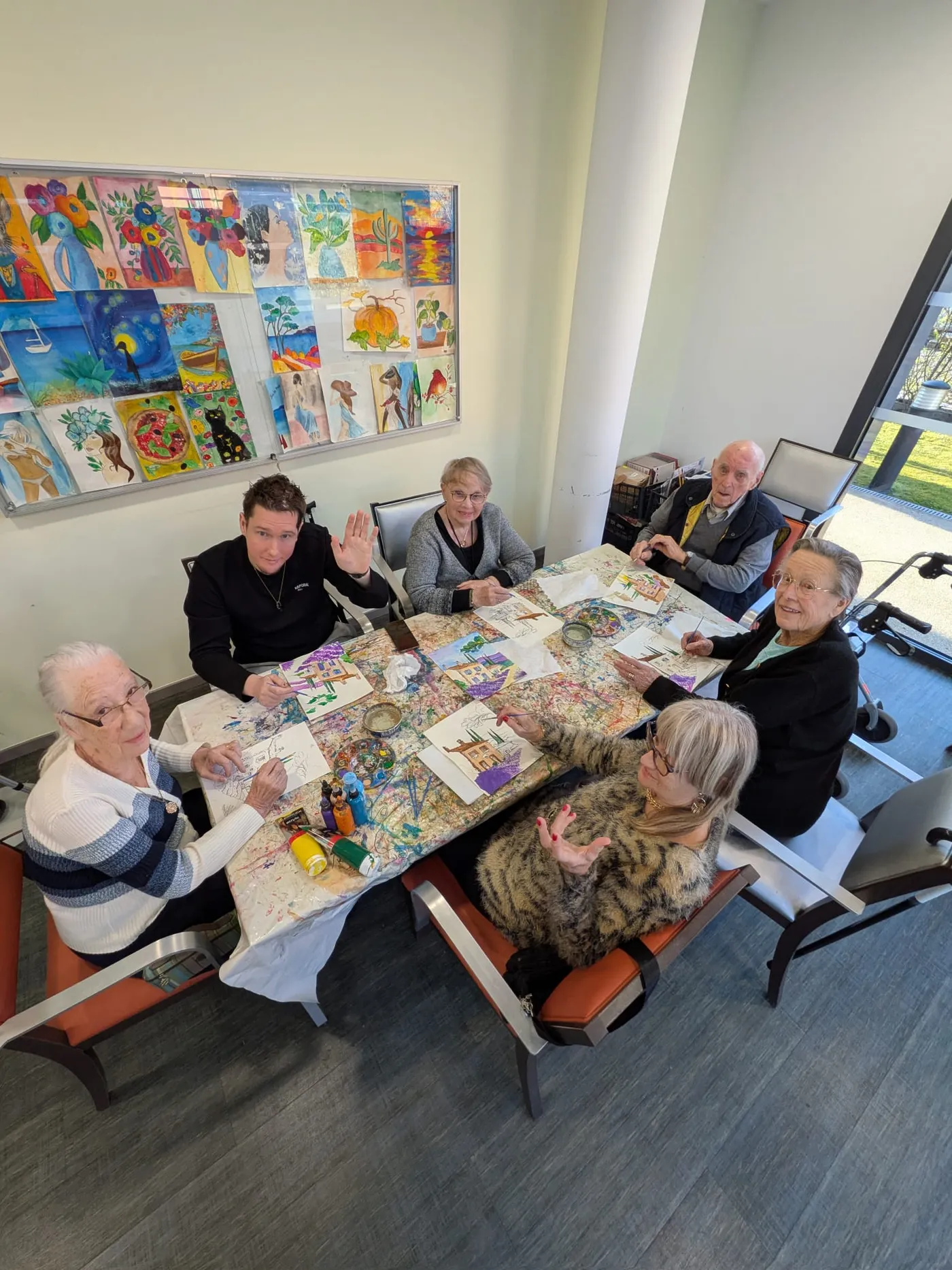 Des résidents et un jeune animateur assemblent des collages colorés autour d'une table, des dessins d'enfants affichés au mur
