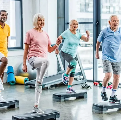 Un groupe de seniors suit un cours de step dans une salle lumineuse, chacun levant un genou au rythme du coach