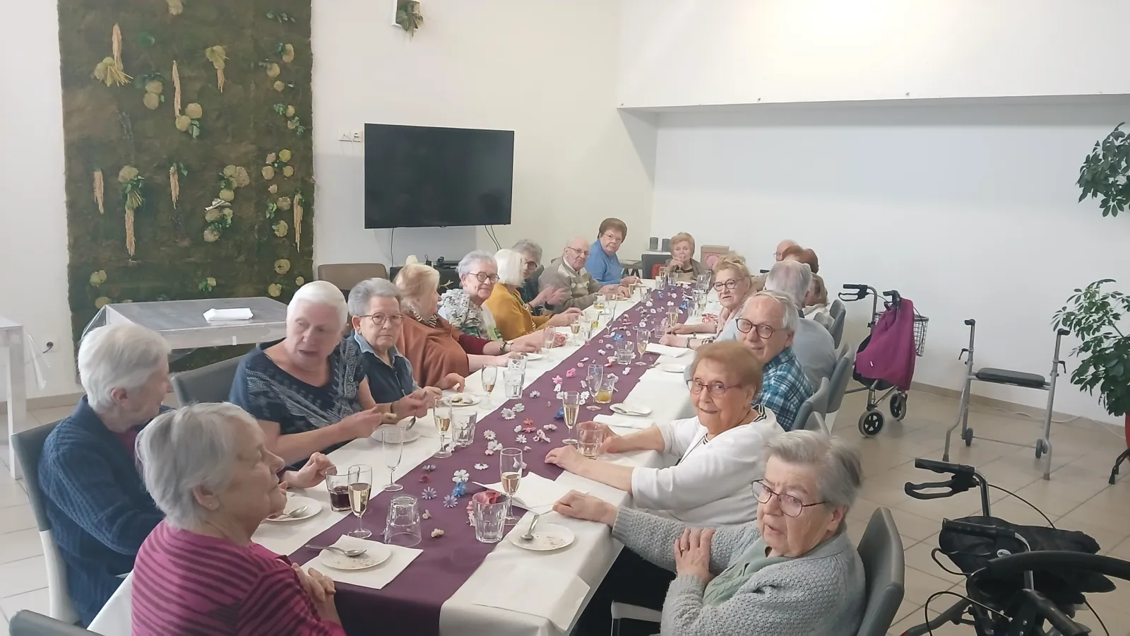 Des résidents installés le long d'une grande tablée habillée d'un chemin de table violet, dans la salle à manger