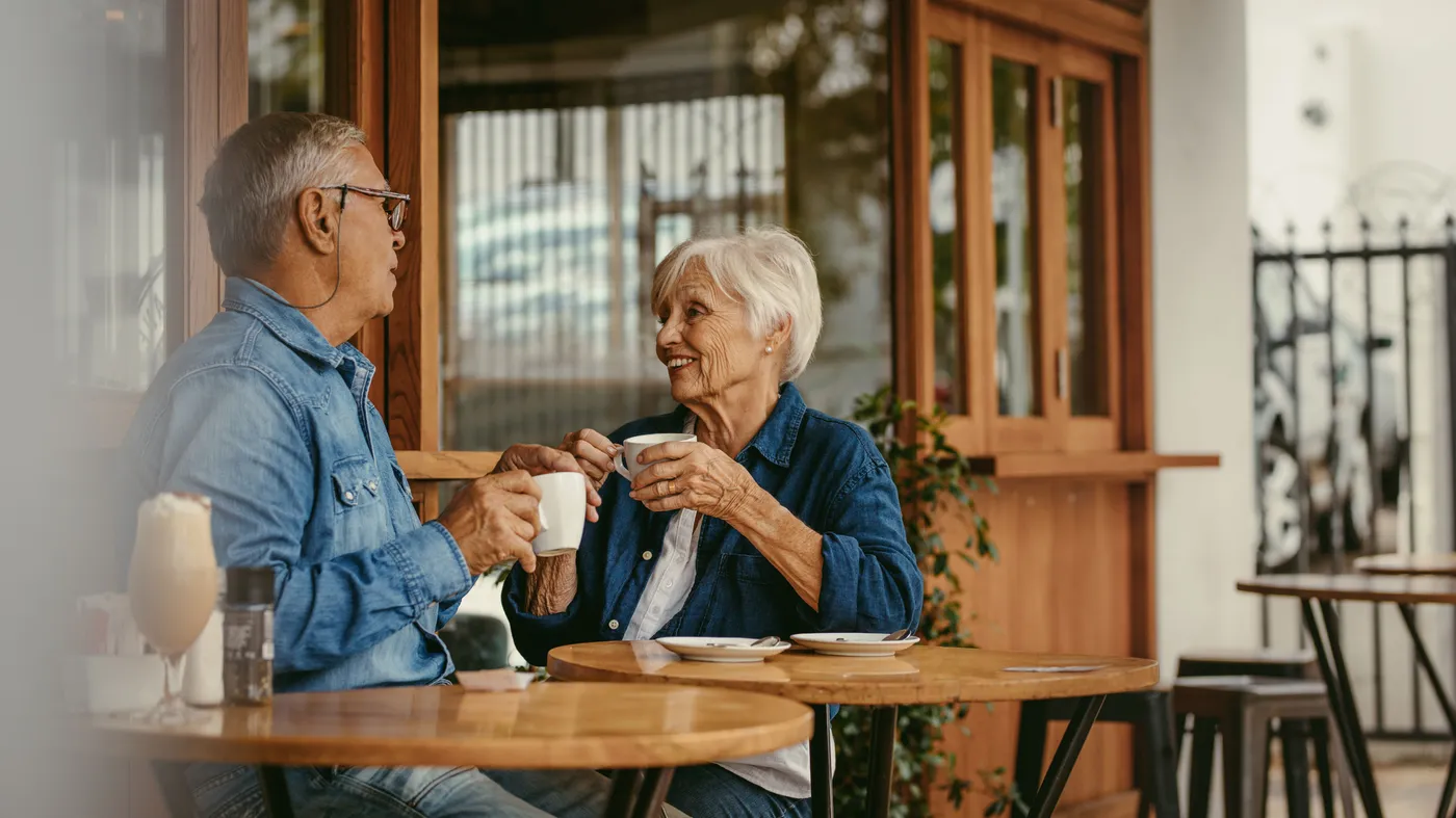 Un couple de seniors attablé à un café, une tasse à la main, en pleine conversation