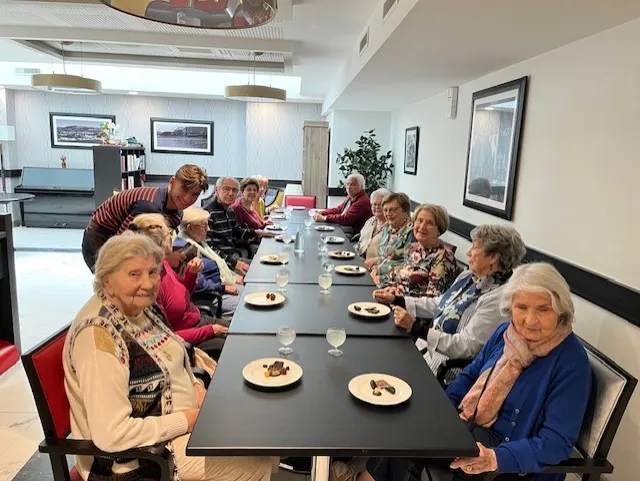 Des résidentes installées le long de la grande table, chacune devant une assiette de chocolats et un verre d'eau