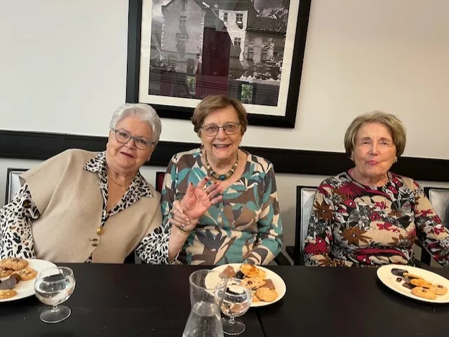 Trois résidentes souriantes à table, des assiettes de douceurs chocolatées devant elles