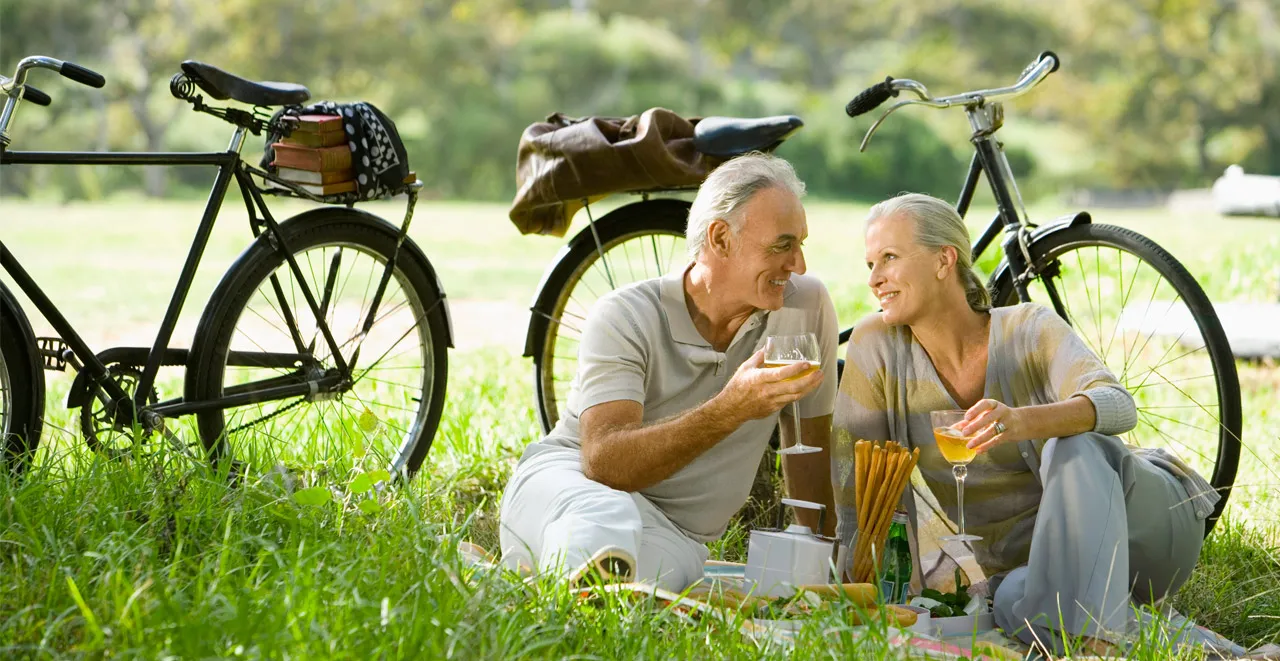 Un couple de seniors pique-nique dans l'herbe à côté de leurs deux vélos posés