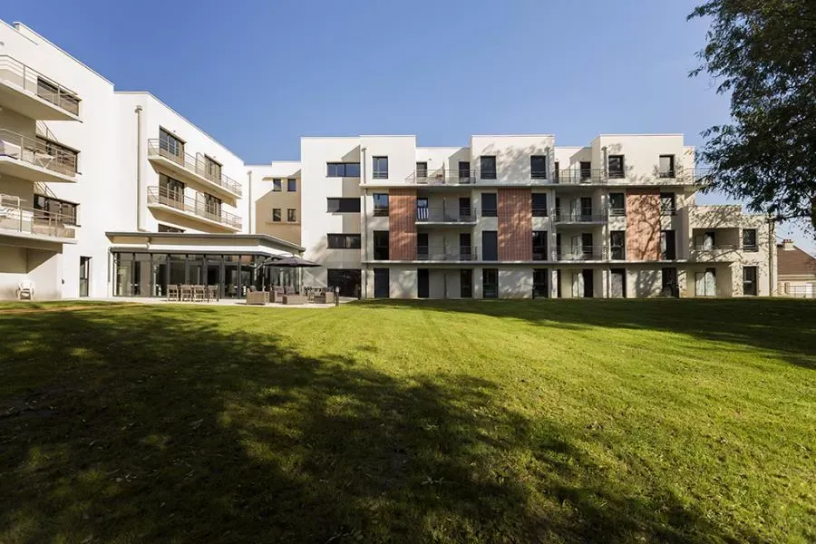 Les ailes à balcons blancs de la résidence vues depuis la pelouse ensoleillée