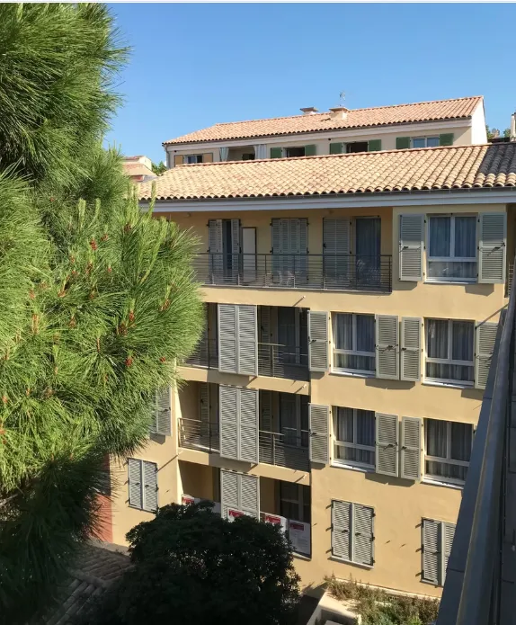 Façade de la résidence seniors OBEO Fréjus, immeuble aux volets clairs bordé d'un pin sous le soleil