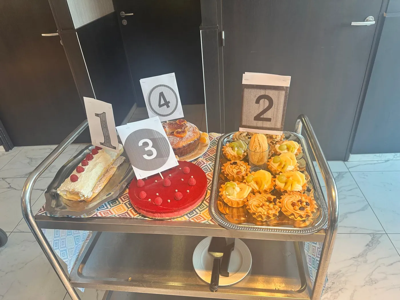 Un chariot de service portant les desserts numérotés, dont le bavarois nappé de framboises