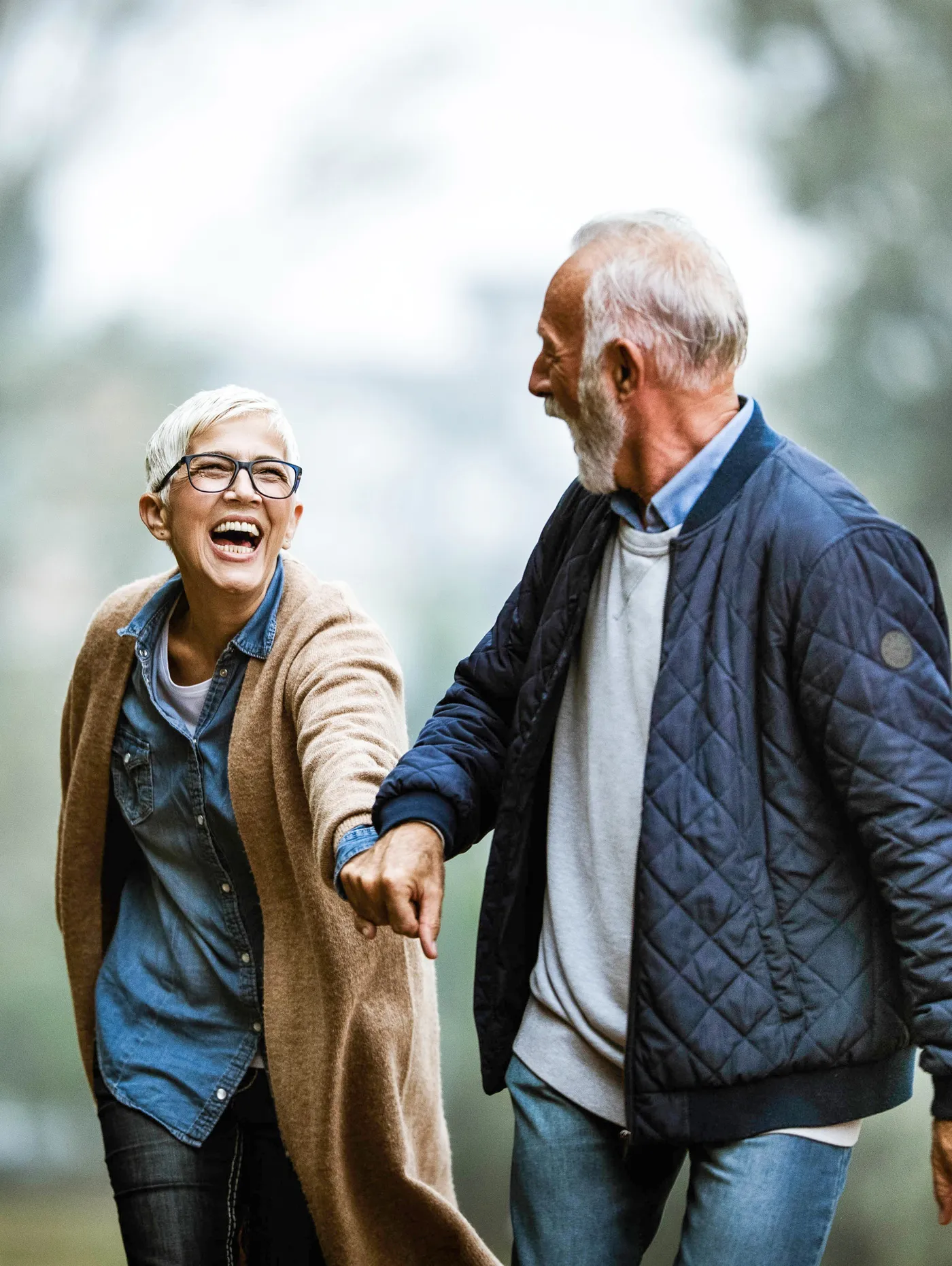 Un couple de seniors rit en marchant, la femme entraînant l'homme par la main