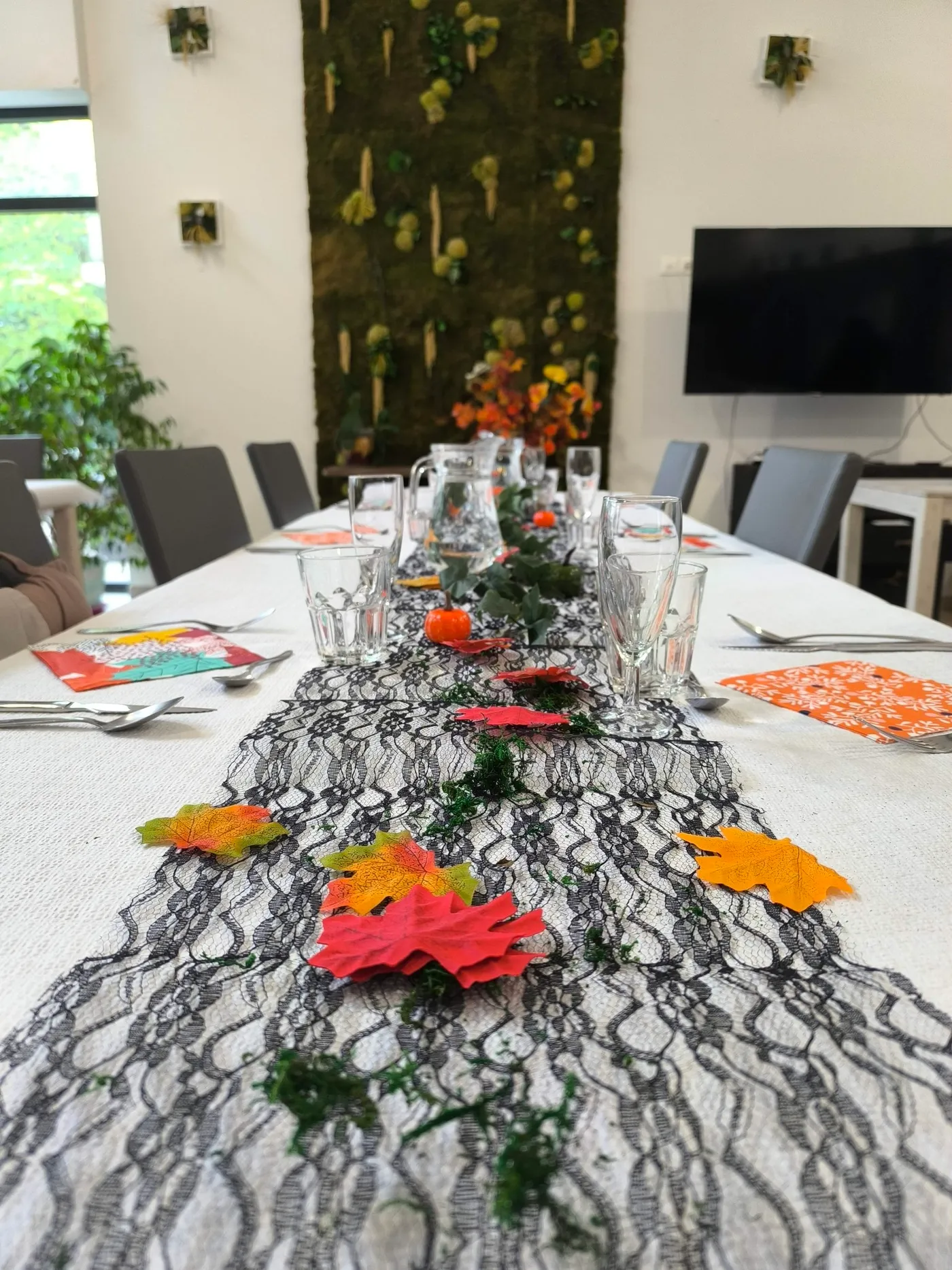 Une longue table habillée de dentelle noire, de feuilles d'automne et de verrerie pour le dîner d'Halloween