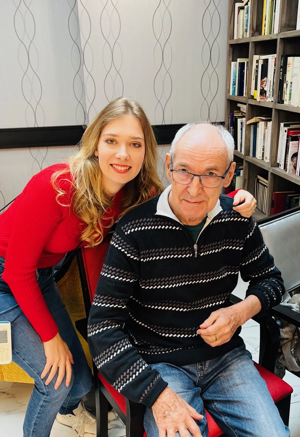 Une jeune bénévole se penche à côté d'un résident pour la photo, dans le coin bibliothèque