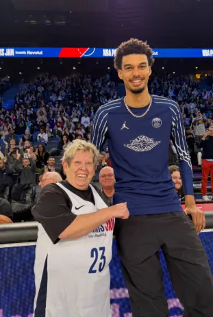 Une supportrice senior pose au bord du terrain avec un grand joueur de basket professionnel