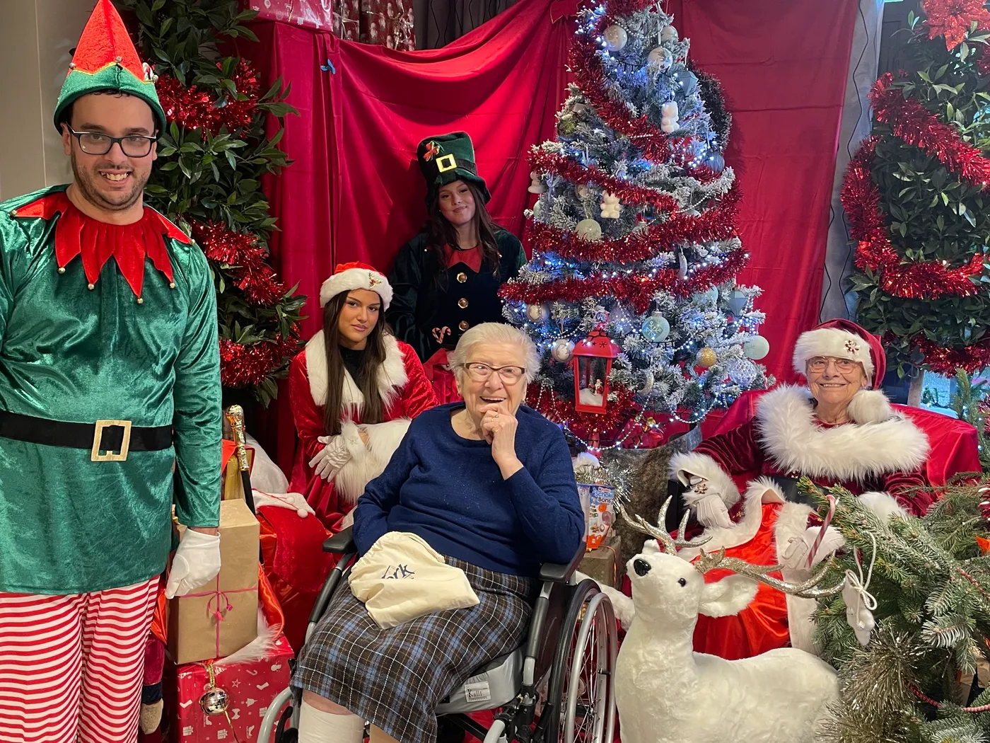 Des membres de l'équipe déguisés en lutins et en Père Noël posent avec une résidente près du sapin décoré