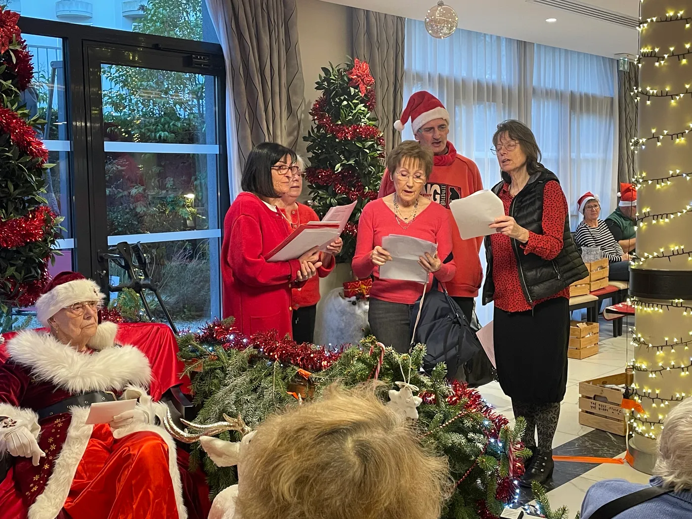 Une chorale en rouge chante des chants de Noël à côté du Père Noël, dans le salon décoré
