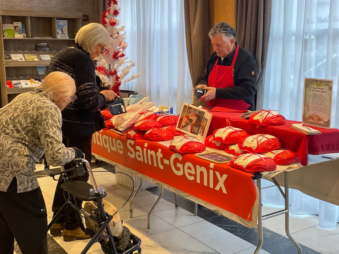 Des résidentes devant le stand de brioches de Saint-Genix, sa nappe rouge couverte de gâteaux ensachés