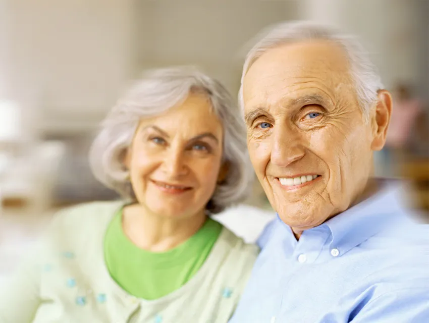Un couple de seniors souriant assis l'un contre l'autre en intérieur