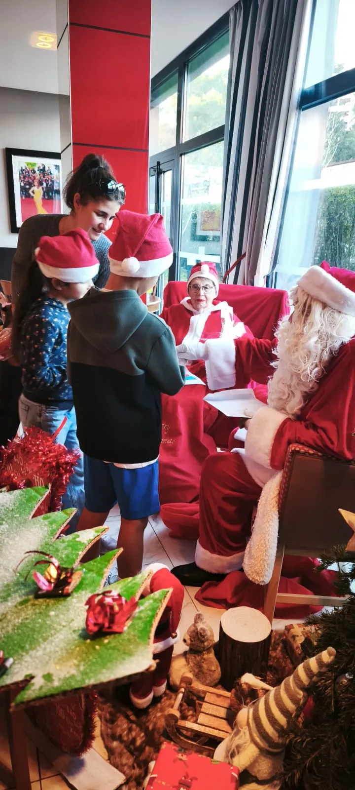 Le père Noël entouré d'enfants et de résidents, à côté de la table des cadeaux