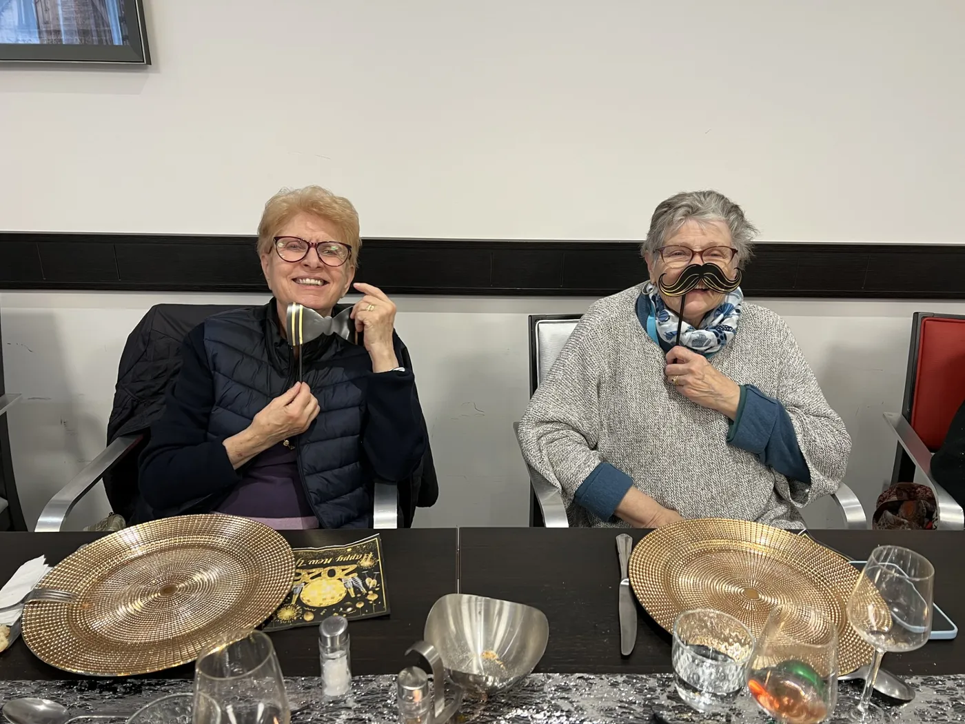 Deux résidentes tiennent des accessoires de photobooth devant leur visage, à table