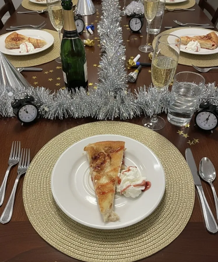 Une assiette de feuilleté doré nappé de crème sur une table du Nouvel An décorée de guirlandes argentées, de petits réveils et d'une bouteille de champagne