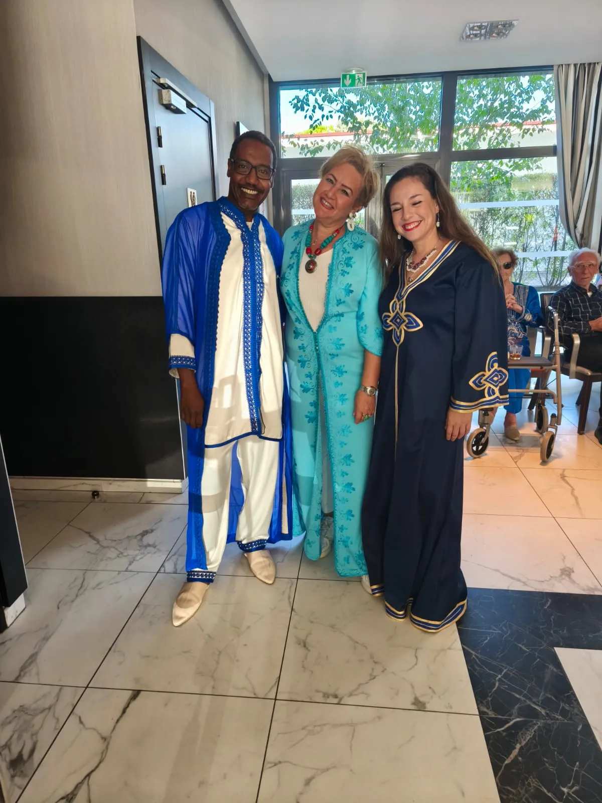 Trois artistes en tenues bleues et turquoise posent ensemble dans le salon