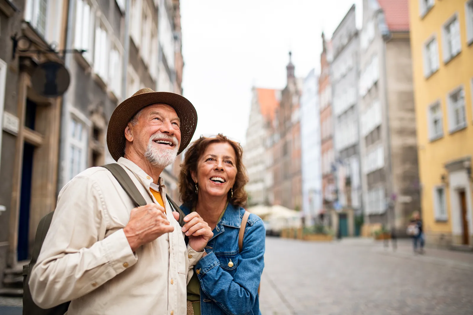 Un couple de seniors marche bras dessus bras dessous dans une rue colorée de vieille ville