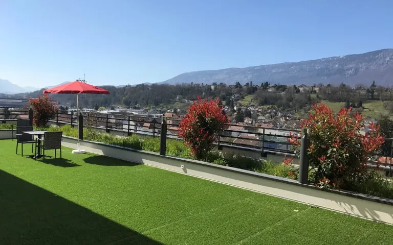 Une terrasse en toiture avec gazon synthétique, parasol et vue sur la vallée jusqu'aux montagnes
