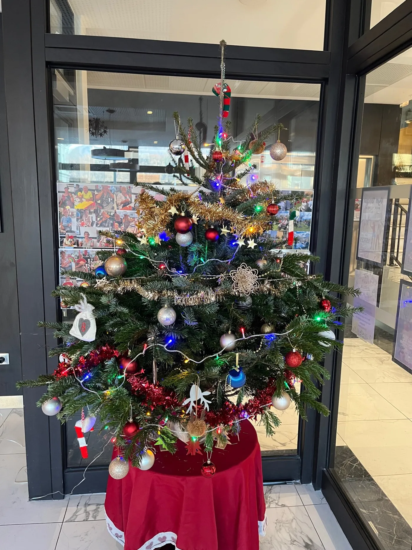 Un sapin de Noël décoré de boules et de guirlandes lumineuses dressé près de la porte vitrée