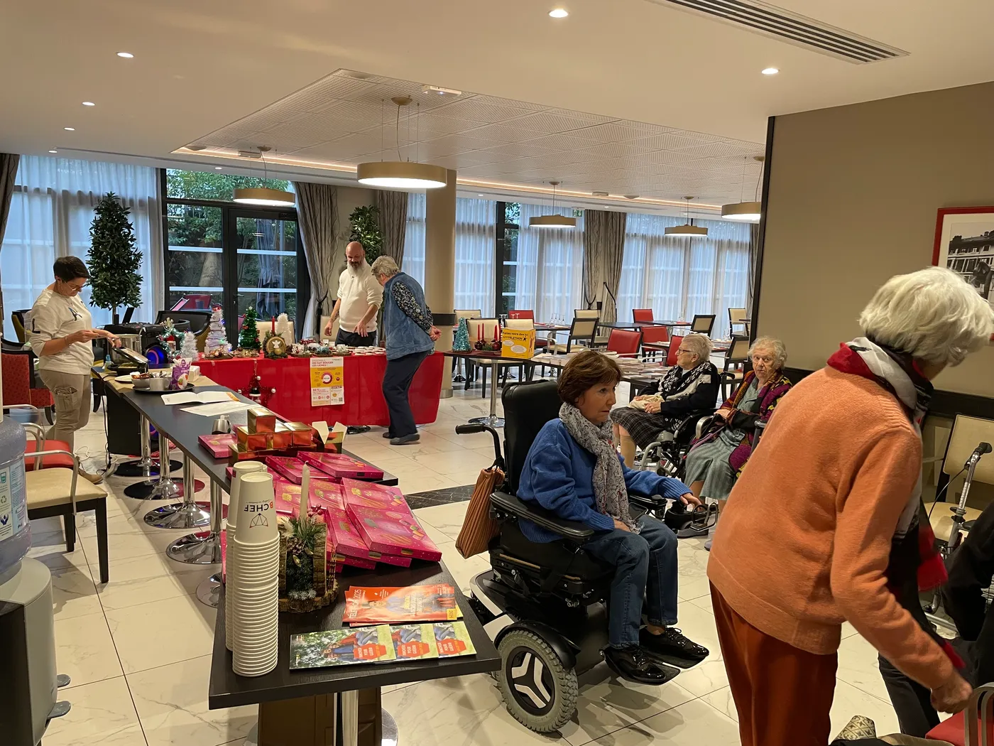 Des résidents parcourent les tables de vente du Téléthon dans le salon