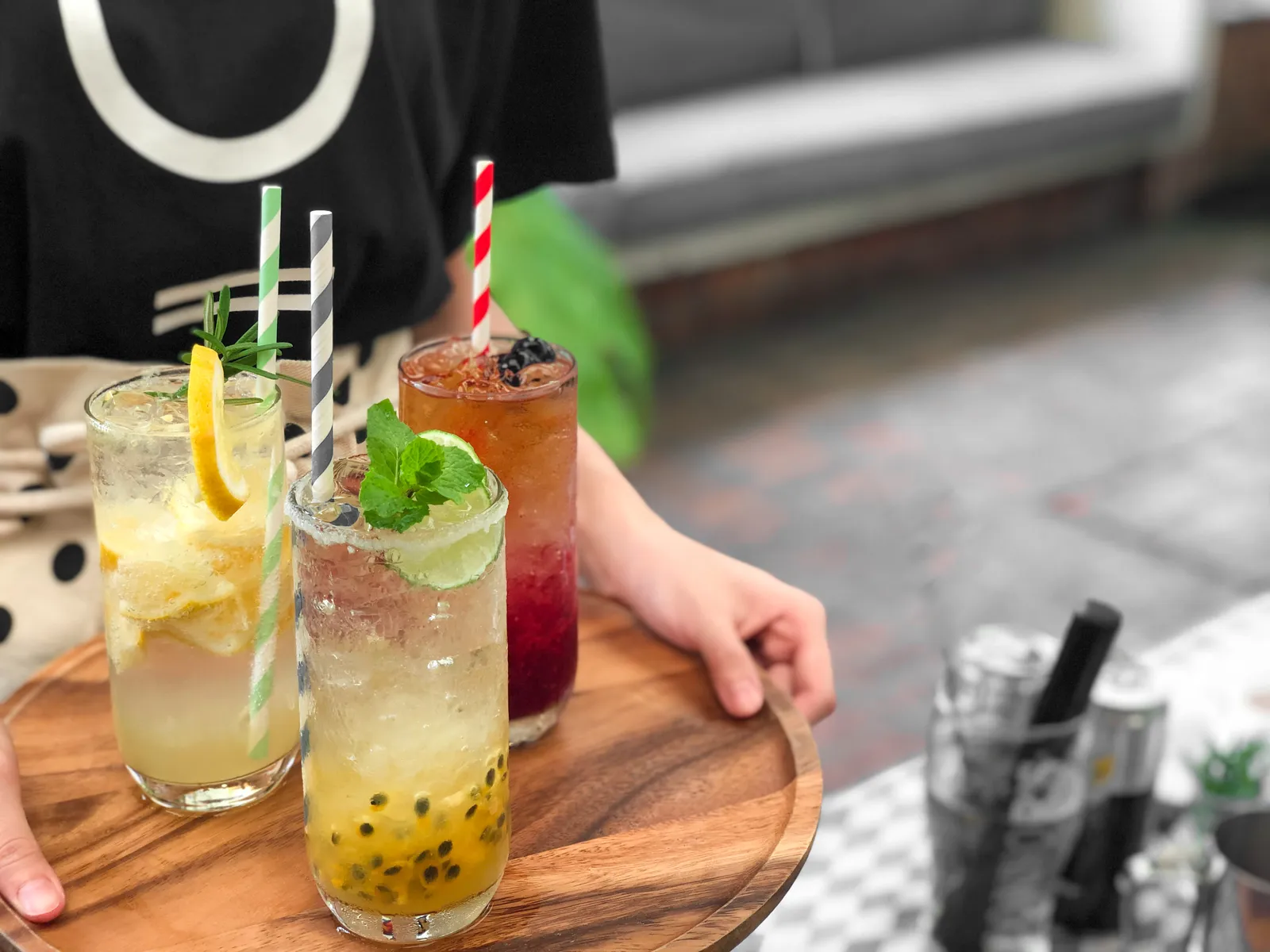 Trois cocktails sans alcool colorés, pailles rayées et fruits frais, présentés sur un plateau en bois