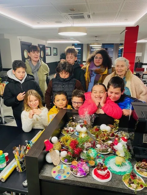 Des écoliers et des membres de l'équipe réunis derrière une table de décorations de Noël faites main