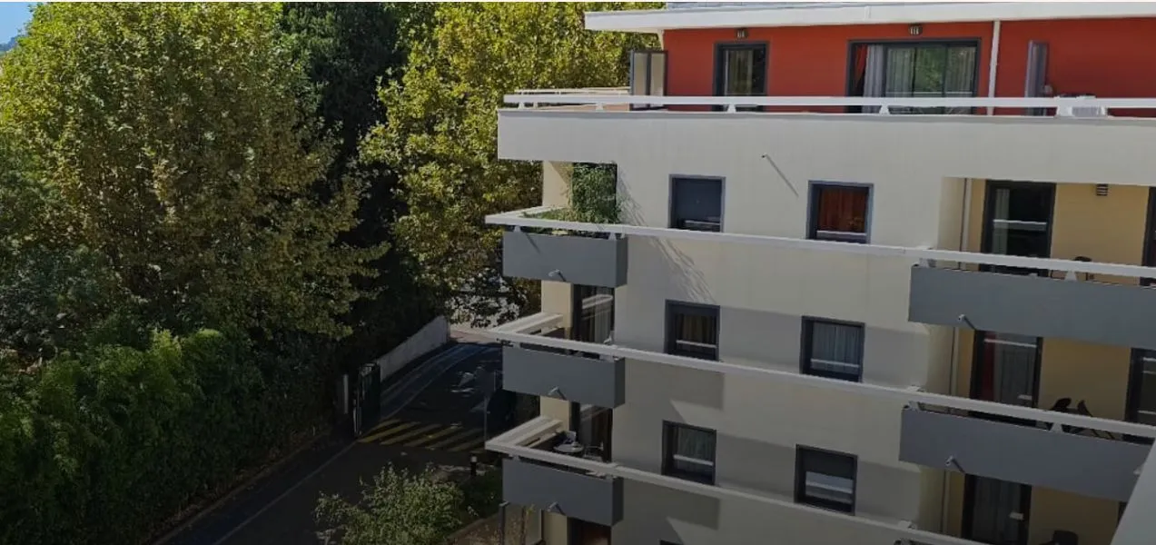 La façade blanche et rouge de la résidence aperçue à travers les arbres