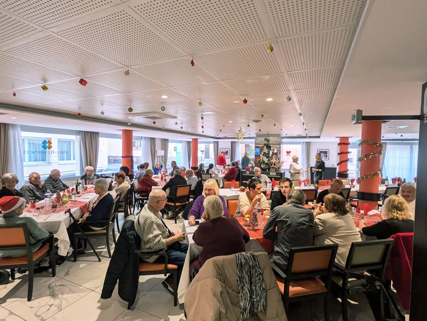 Une salle à manger pleine de convives pour le repas de Noël, des décorations suspendues au plafond