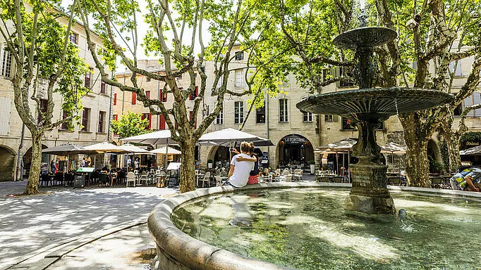 La fontaine et les terrasses ombragées d'une place d'Uzès