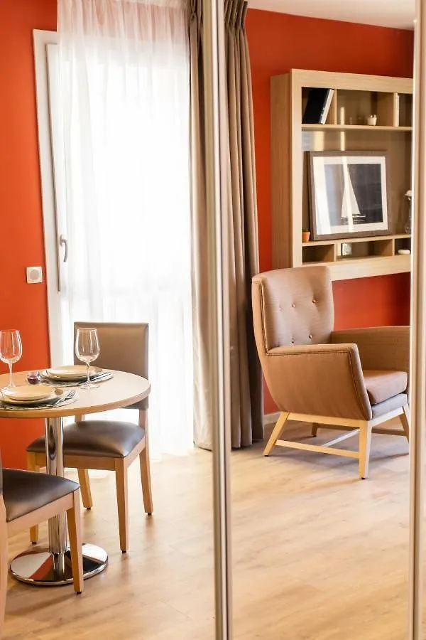 Un appartement au mur orange, avec une table dressée et des fauteuils près de la fenêtre
