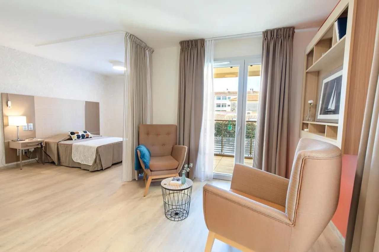 Appartement meublé de la résidence OBEO Fréjus : coin nuit séparé par un rideau, deux fauteuils autour d’une table basse et porte-fenêtre ouvrant sur un balcon.