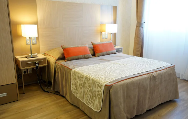 Chambre d’un appartement témoin d’Uzès : lit deux places, liseuses murales et tables de chevet devant un voilage lumineux