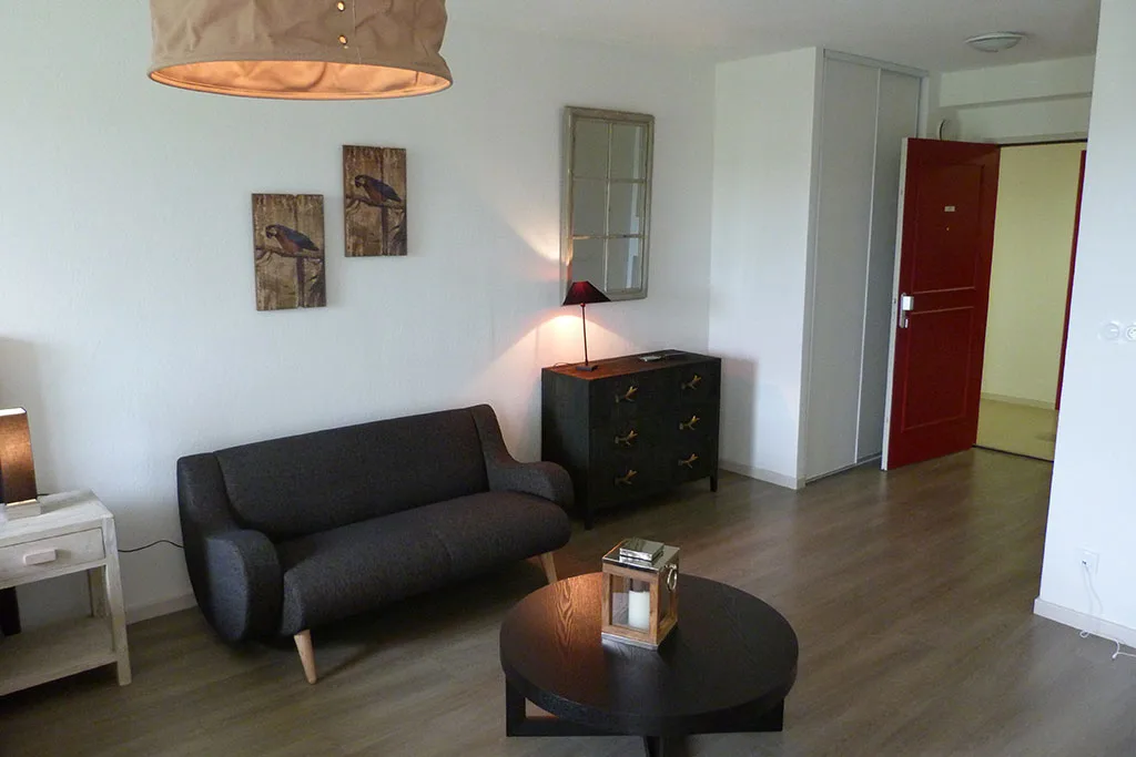 Coin salon d’un appartement témoin d’Yzeure : canapé anthracite, table basse ronde, commode et lampe sur pied dans une pièce claire